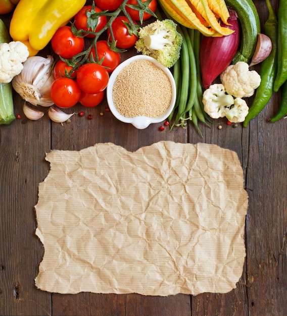 Grano de amaranto crudo en un recipiente y verduras sobre madera