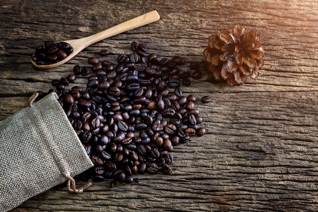 Grano de café en cuchara y bolsa sobre fondo de madera