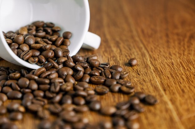 Grano de café saliendo de una taza blanca sobre la mesa de madera