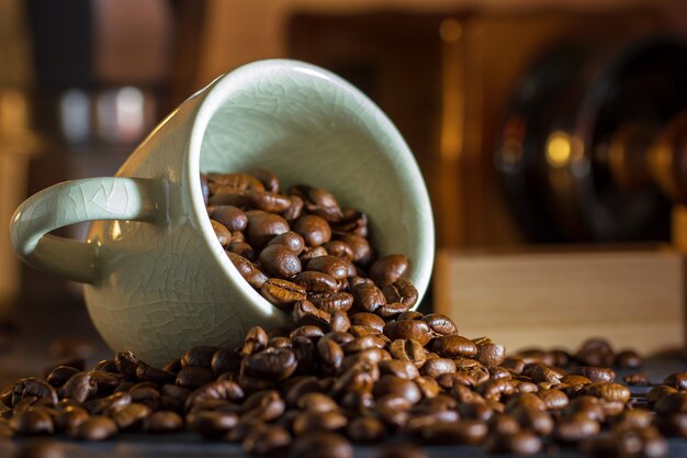 Grano de café en la taza blanca y molinillo de café en la mesa de madera. Concepto desayuno o café en la mañana.