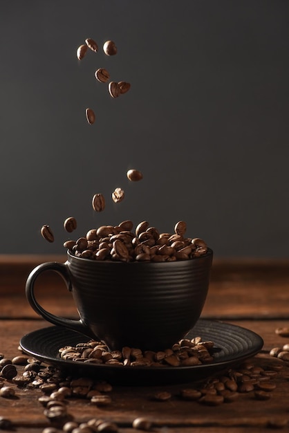 Grano de café y taza negra que caen granos de café en una taza negra sobre madera rústica estilo comida oscura foto enfoque selectivo