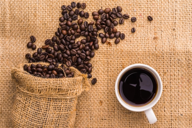 grano de café tostado en tela de saco y café negro caliente de cerca.