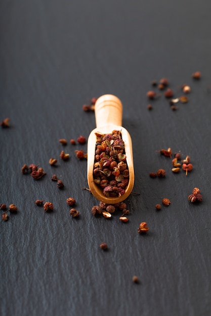 Grano de pimienta chino, pimienta de Sichuan en cuchara de madera en placa de piedra de pizarra negra con espacio de copia