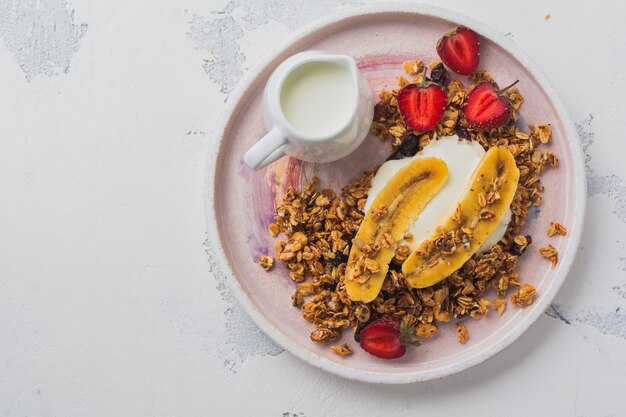 Foto granola de avena con yogur, fresas frescas y plátano, semillas de chía, girasol y miel en placa de cerámica blanca sobre fondo claro. vista superior.