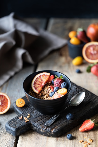 Granola caseira com frutas frescas, frutas no café da manhã. O conceito de alimentação saudável. Mesa de madeira. Fundo escuro