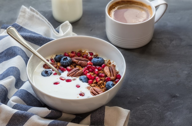 Granola caseira com sementes de romã, mirtilo, noz-pecã e iogurte em fundo cinza de concreto