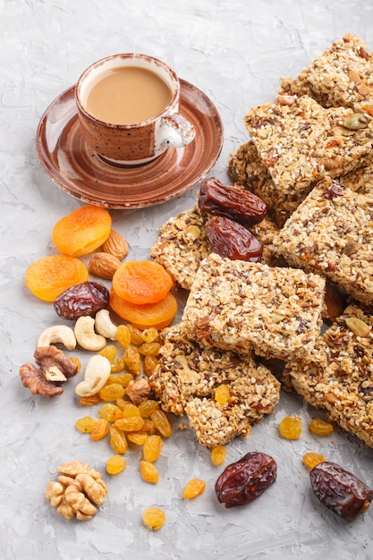 Granola caseira de flocos de aveia, tâmaras, damascos secos, passas, nozes com uma xícara de café sobre um fundo cinza de concreto