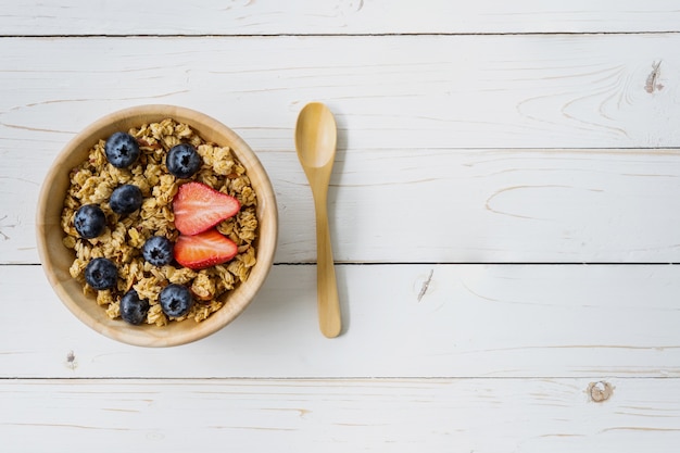 Granola caseira e bagas frescas na mesa de madeira com espaço.