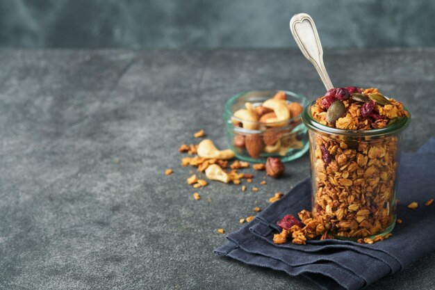 Granola caseira em frasco de vidro com iogurte grego ou leite e castanha de caju amêndoas abóbora com sementes de cranberry secas em fundo de mesa cinza escuro Energia saudável café da manhã ou lanche Vista superior