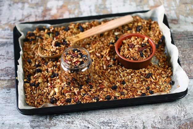 Granola caseira recém-feita em uma assadeira com uma colher de pau e potes