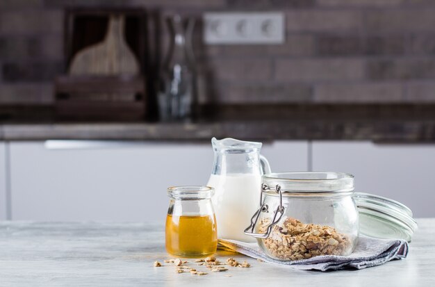 Granola caseiro, leite ou, e mel no fundo da tabela na cozinha. Copie espaço