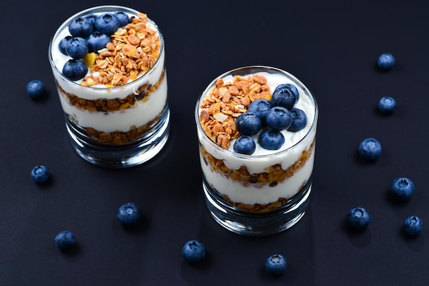 Granola casera al horno con yogur y arándanos en un vaso sobre fondo negro Espacio para texto o diseño