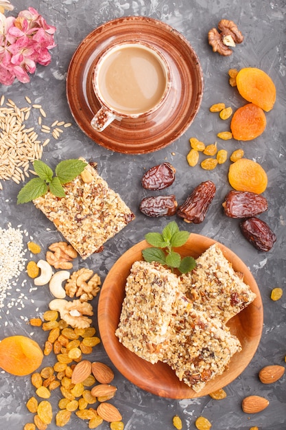 Granola casera de copos de avena, dátiles, albaricoques secos, pasas, nueces con una taza de café sobre una superficie de hormigón negro. Vista superior.