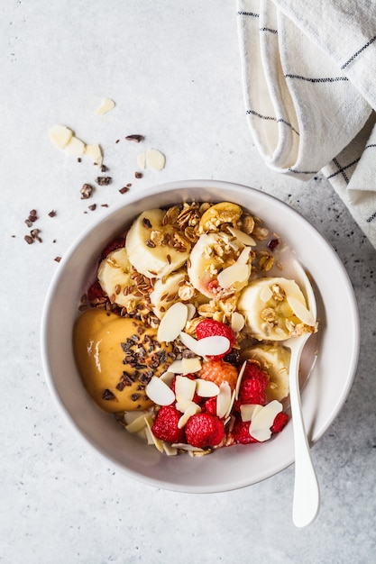 Granola com frutas, banana, manteiga de amendoim e chocolate em uma tigela branca.