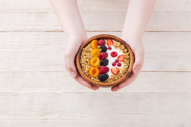 Granola com frutas e mão na mesa de madeira branca