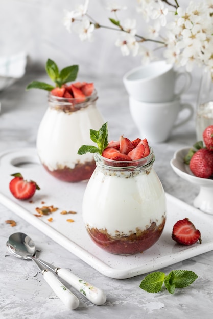 Granola com iogurte e morangos em uma jarra de vidro.