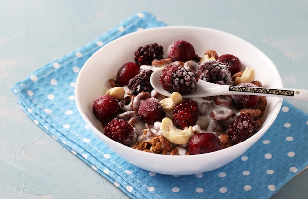 Granola crocante com iogurte natural, cereja congelada e amora, chocolate e nozes em uma tigela branca sobre fundo azul. Fechar-se