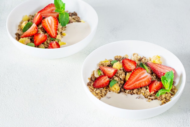 Granola crujiente casera con nueces, frutas secas, fresas frescas, menta y yogur (leche horneada fermentada) en un plato blanco.