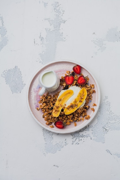 Granola de aveia com iogurte, morango fresco e banana, sementes de chia, girassol e mel na placa de cerâmica branca sobre fundo claro. vista do topo.