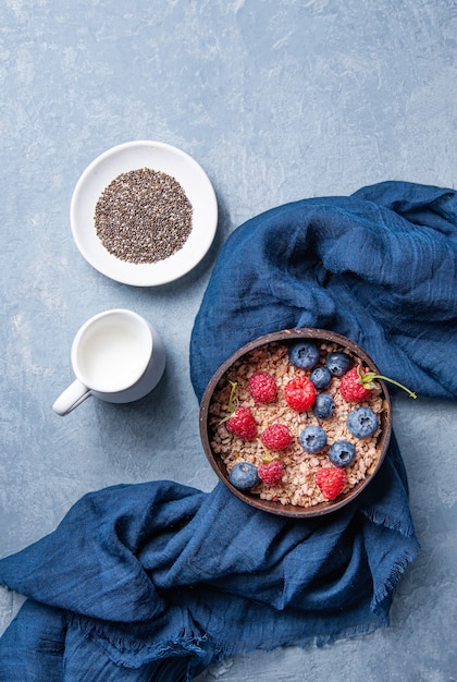 Granola energética com framboesa, mirtilo e leite em uma tigela de coco no azul