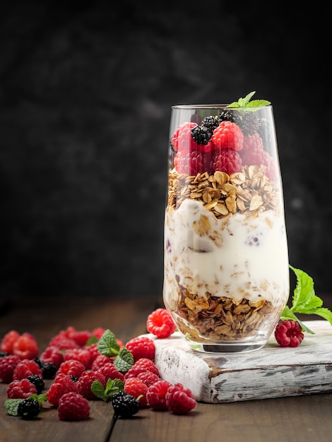 Granola con frambuesas y moras en un vaso con yogur sobre fondo oscuro