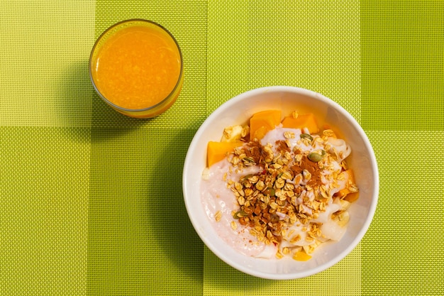 Granola, frutas, tigela de iogurte e suco de laranja sobre fundo verde. Conceito de café da manhã saudável
