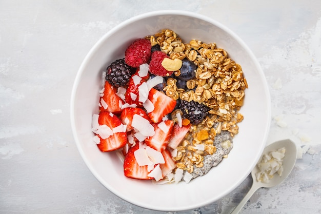 Granola con leche, chia, bayas y mantequilla de maní en un tazón blanco, vista superior.