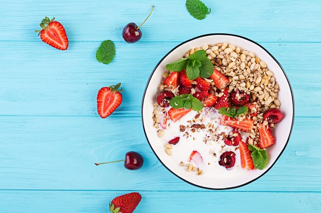 Granola, morangos, cereja, nozes e iogurte em uma tigela sobre uma mesa de madeira