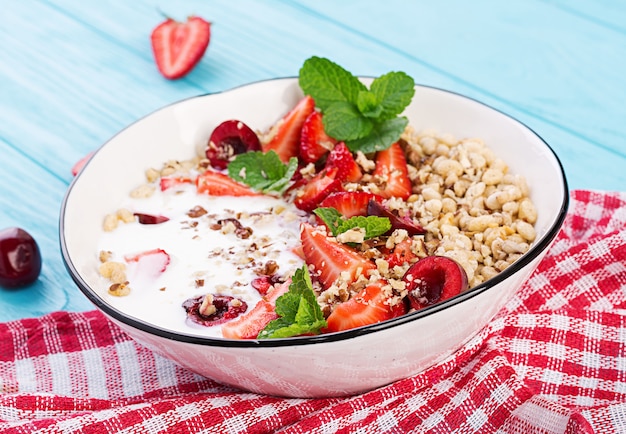 Granola, morangos, cereja, nozes e iogurte em uma tigela sobre uma mesa de madeira