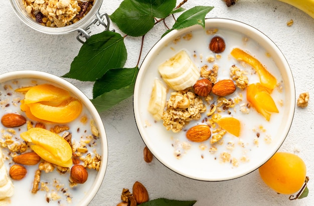 Granola-Müsli mit Früchten, Nüssen und Milch in Schüssel auf weißem Hintergrund. Gesunde Frühstückszerealien Draufsicht