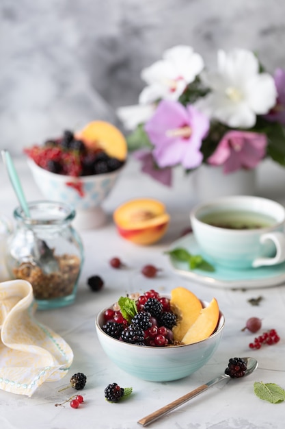 Granola o muesli con frutas y bayas para un desayuno saludable en la mañana con un ramo de flores de verano en una mesa de luz.