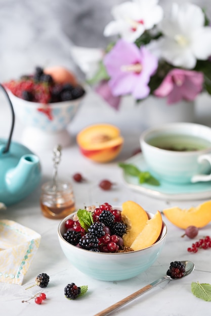 Granola o muesli con frutas y bayas para un desayuno saludable en la mañana con un ramo de flores de verano en una mesa de luz.