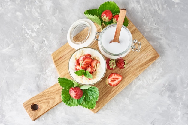 Granola o yogurt con fresa en vidrio, bayas frescas y frasco con azúcar en una tabla de cortar, vista superior