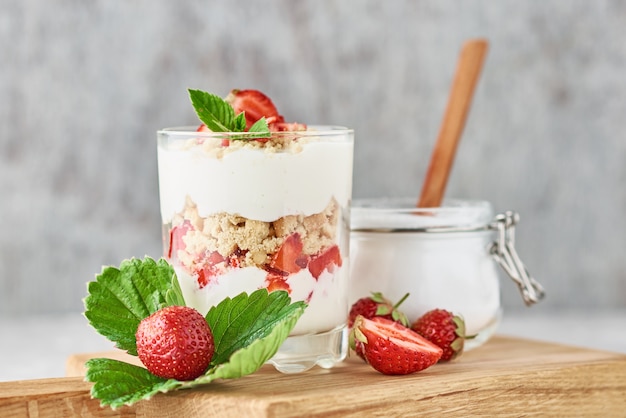 Granola ou iogurte com morango em vidro, frutas frescas e jar com açúcar sobre uma tábua