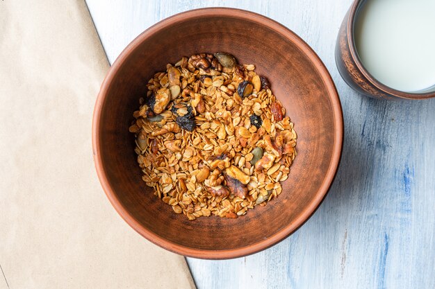 Granola en un recipiente de arcilla marrón con un vaso de leche. Desayuno sabroso y saludable.