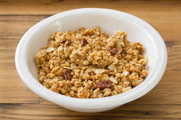 Granola en tazón blanco sobre superficie de madera marrón