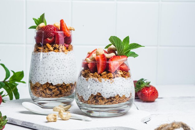 Granola con yogur chia y fresas en un vaso sobre un fondo blanco.