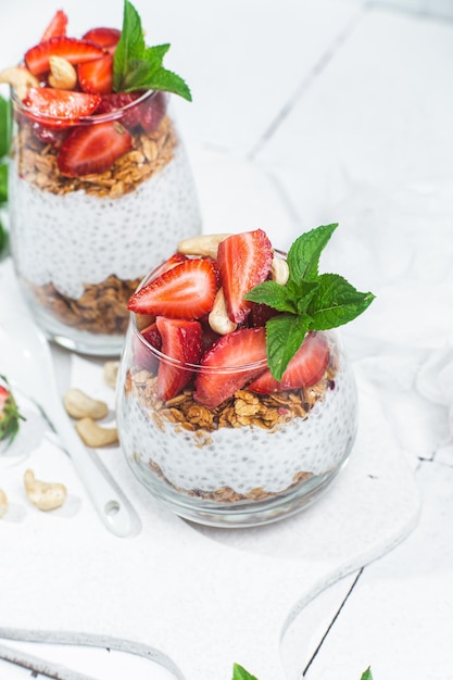 Granola con yogur chia y fresas en un vaso sobre un fondo blanco.