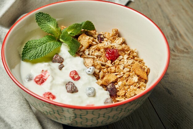 Granola con yogur griego y bayas en un recipiente con tela de lino sobre una superficie de madera. Cerrar con lugar para el texto. Desayuno clásico