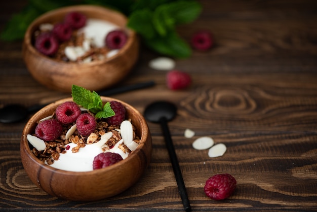 Granola con yogur griego, menta y frambuesas en tazón de madera