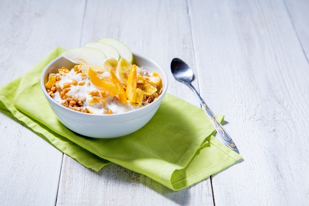 Foto granola y yogur vegetariano con rodajas de manzana, albaricoque, plátano sobre una superficie de madera blanca. concepto de desayuno saludable
