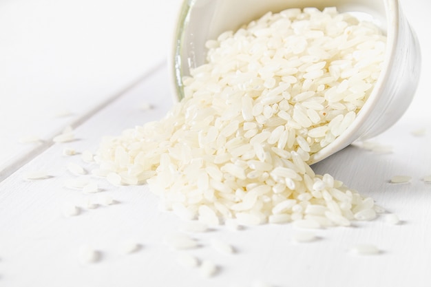 Granos del arroz blanco crudo en una tabla de madera blanca de tableros. Ingredientes para cocinar.