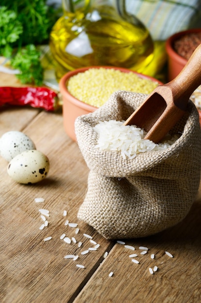 Granos de arroz orgánico en saco de arpillera en la mesa de la cocina con ingredientes alimentarios