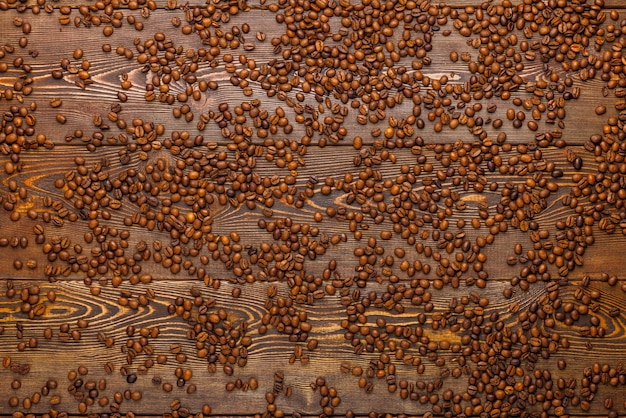 Granos de café asados esparcidos sobre una tabla de madera - fondo de marco completo vista de ángulo alto