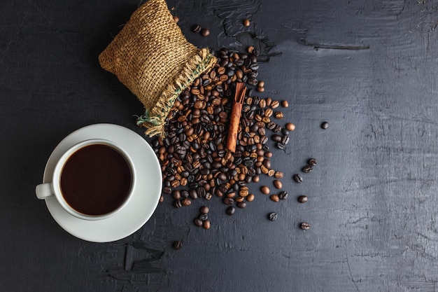 Granos de café en bolsa de saco marrón con taza de café sobre fondo negro