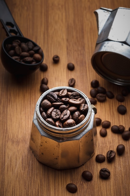 Granos de café en una cafetera géiser sobre una mesa de madera.