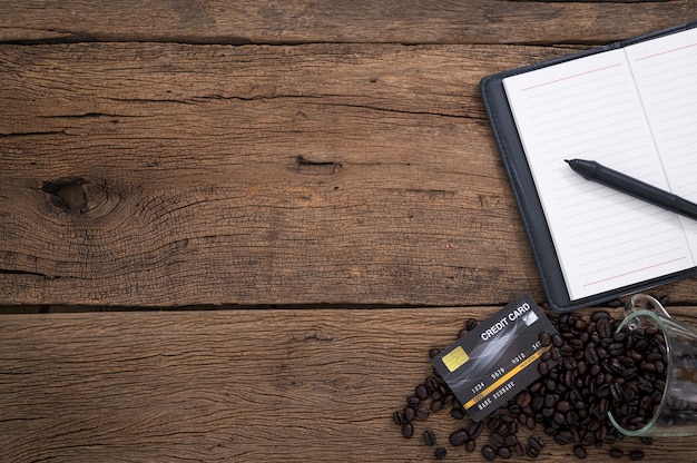 Los granos de café del cuaderno de la tarjeta de crédito colocados en una vista superior de la mesa de madera