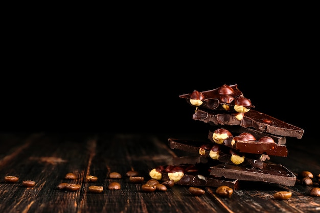 Granos de café dispersados y chocolate negro en una tabla de madera.