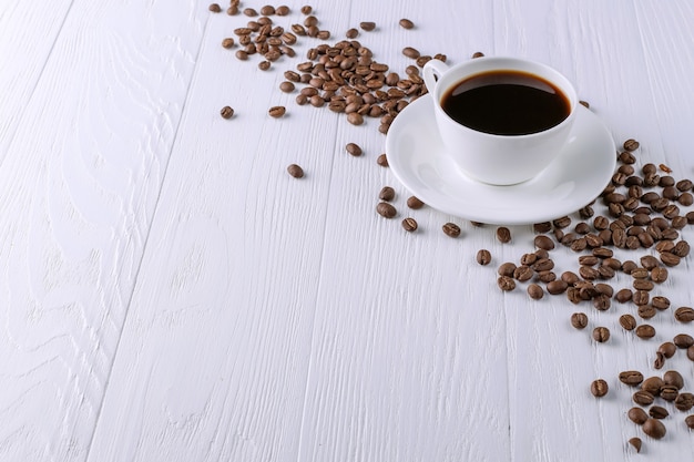 Granos de café dispersados, una taza y chocolate negro en una tabla de madera blanca. Copia espacio
