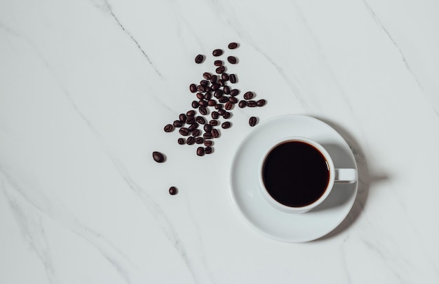 Granos de café dispersos y una taza de café espresso sobre fondo de mármol